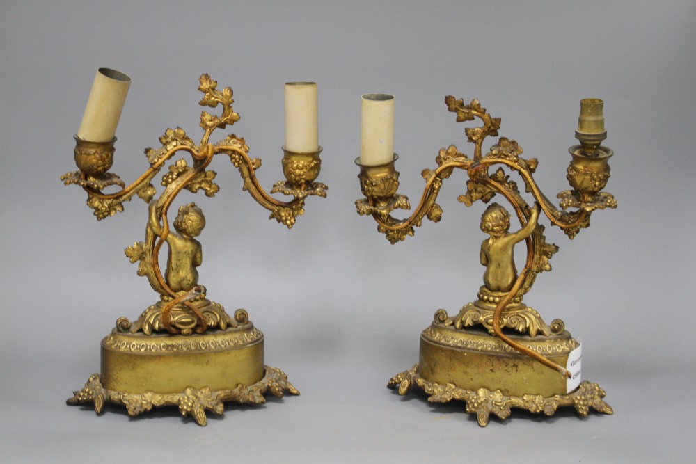 A pair of French gilt metal two light candelabra, modelled with putti seated beneath vine branches and inset with Sevres style